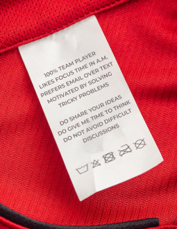 Close up of a clothing label that reads: "100% team player, likes focus time in A.M. prefers email over text, motivated by solving tricky problems. Do Share your Ideas, Do give me time to think, Do not avoid difficult discussions"