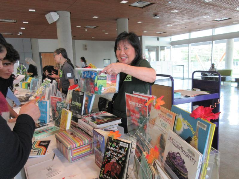 Woman smiling at camera holds a box of snacks in front of a table with book displays.